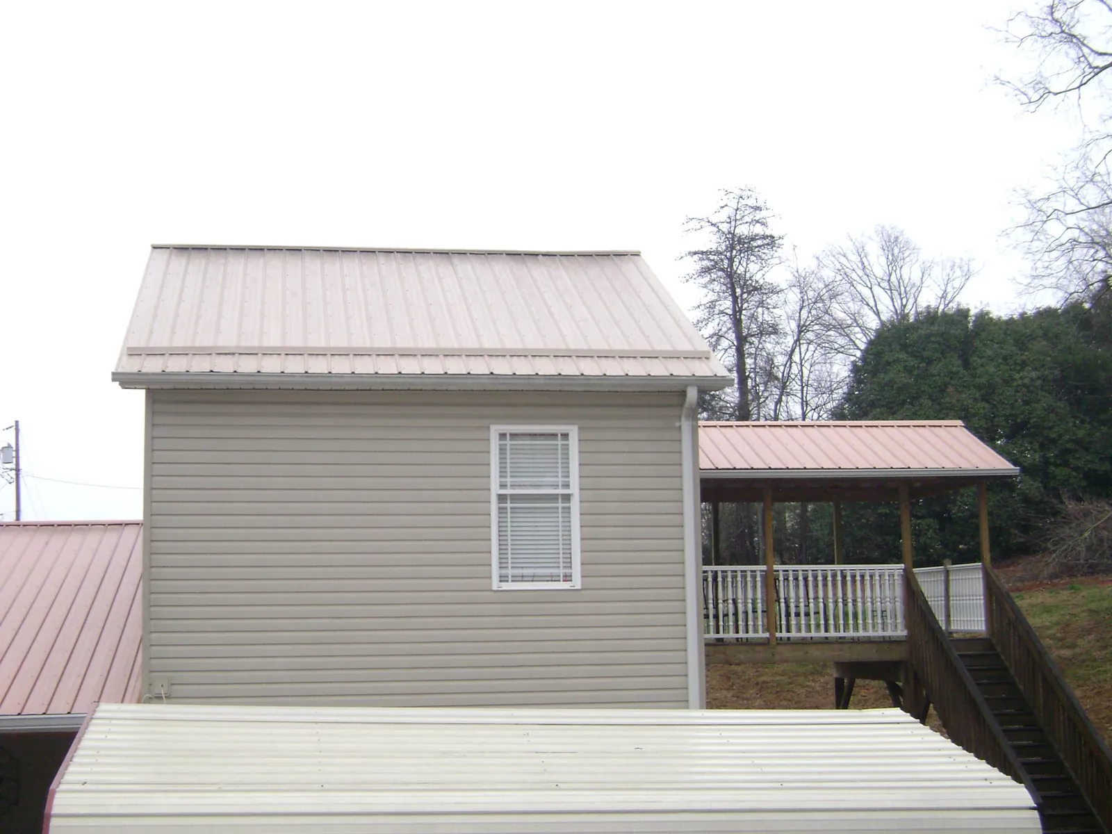Tan metal roofs on a two story addition and attached porch, from a Roof Replacement job in Webster